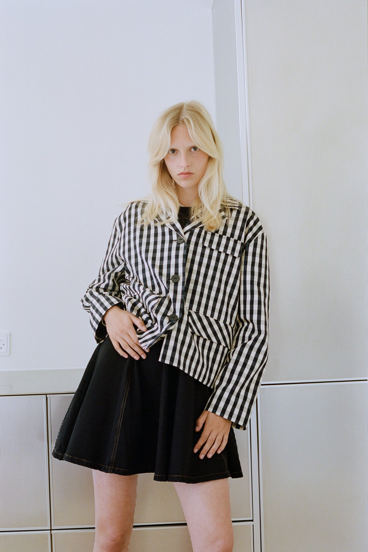 Campaign portrait of a model wearing a black-and-white checked button-front shirt with a dark denim skirt.