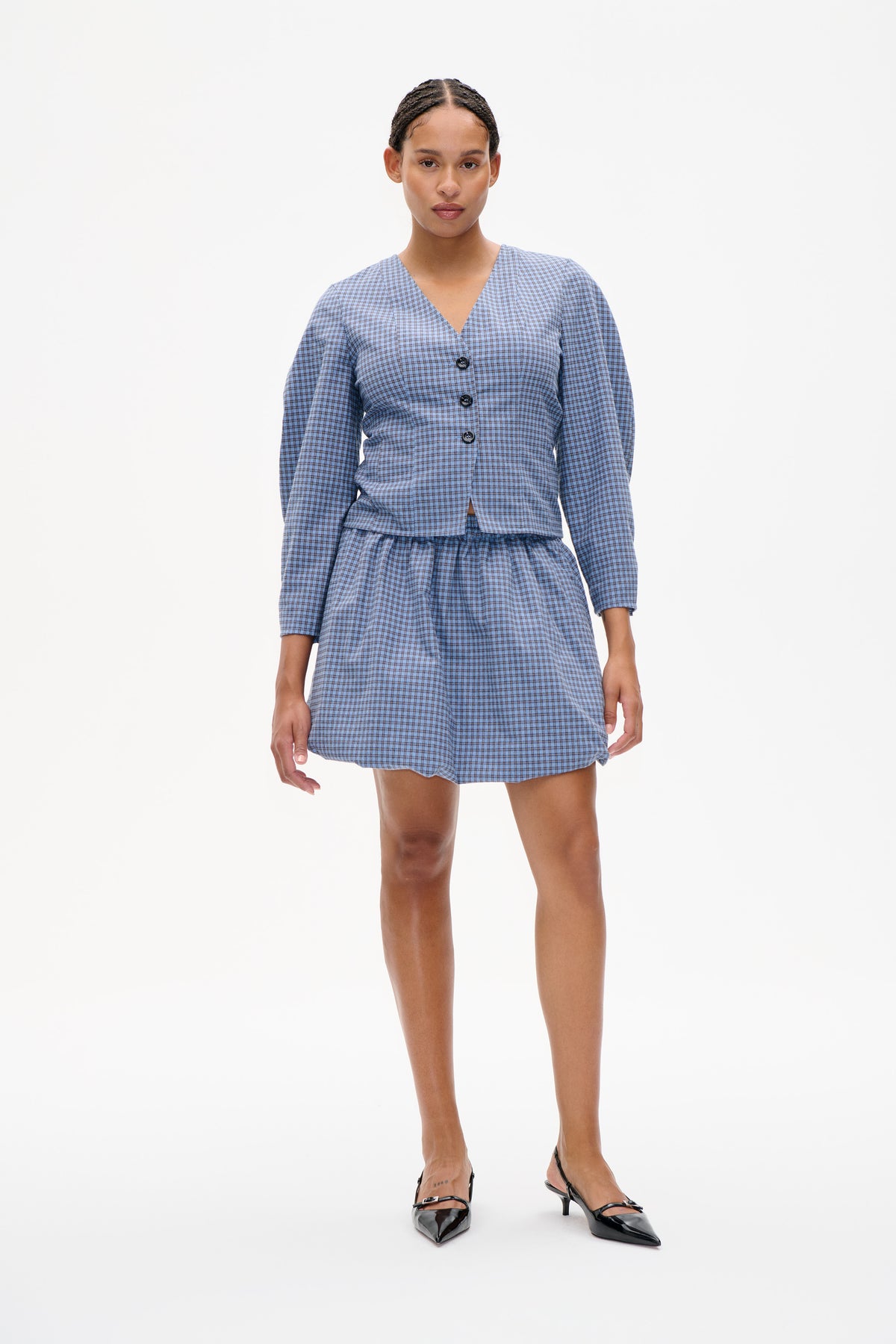 Front view of a model wearing a blue checked V-neck button-front top with long sleeves and a matching gathered mini skirt.