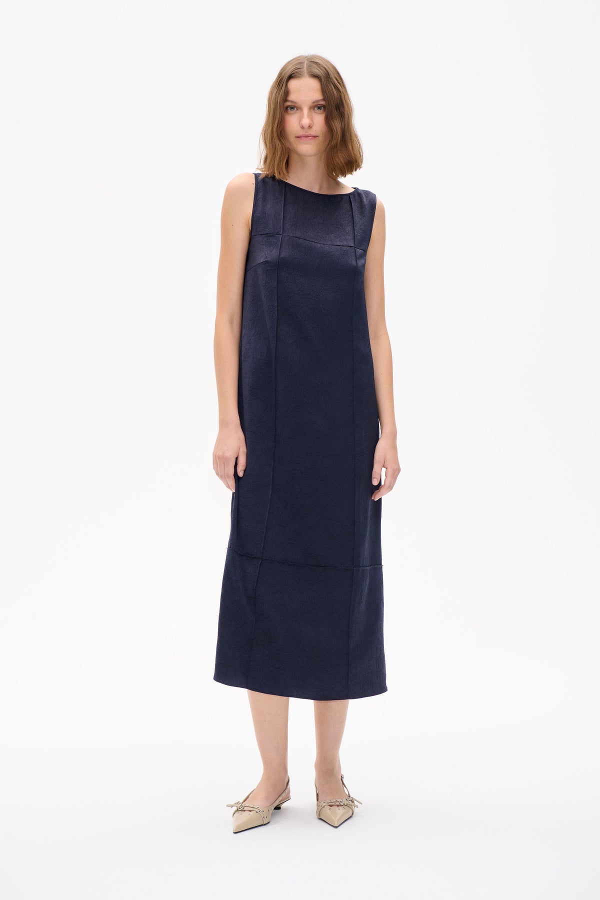 Front view of a model wearing a sleeveless navy dress with a subtle textured pattern and panel seams.