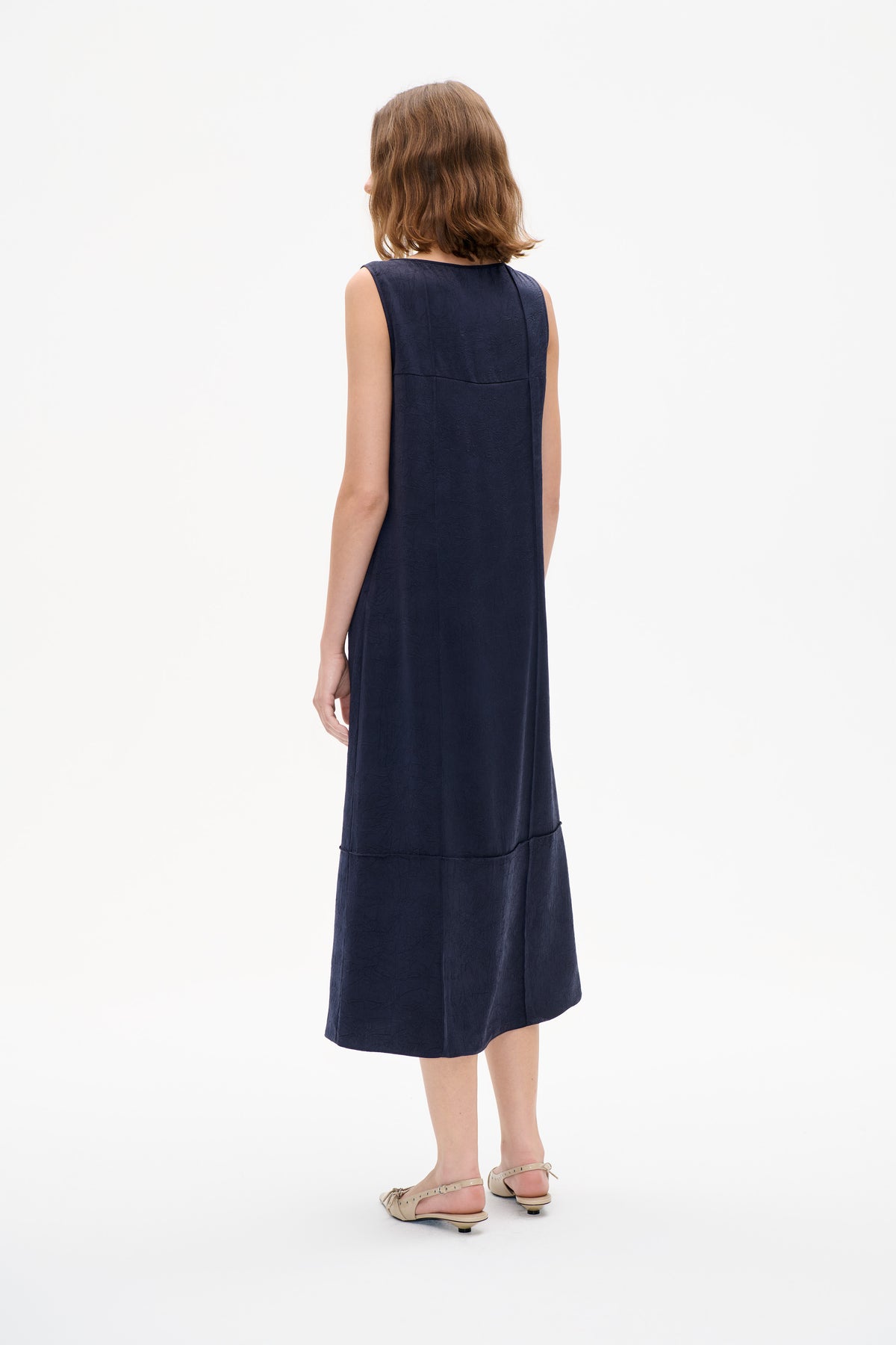 Back view of a sleeveless navy midi dress with subtle raised texture and horizontal panel seams.