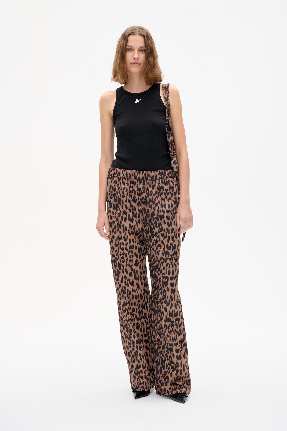Model wearing a black sleeveless top with a small white logo and brown-and-black leopard-print wide-leg trousers, shown from the front.