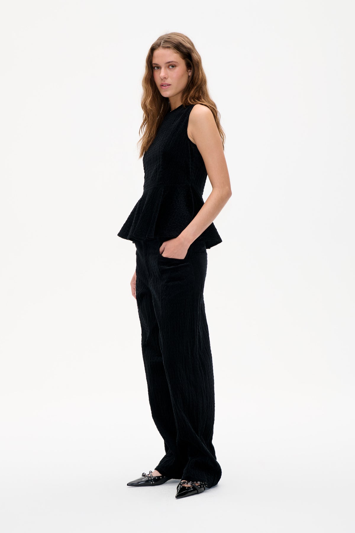 Model wearing a black sleeveless textured peplum top with matching wide-leg trousers, shown from the front against a white studio background.