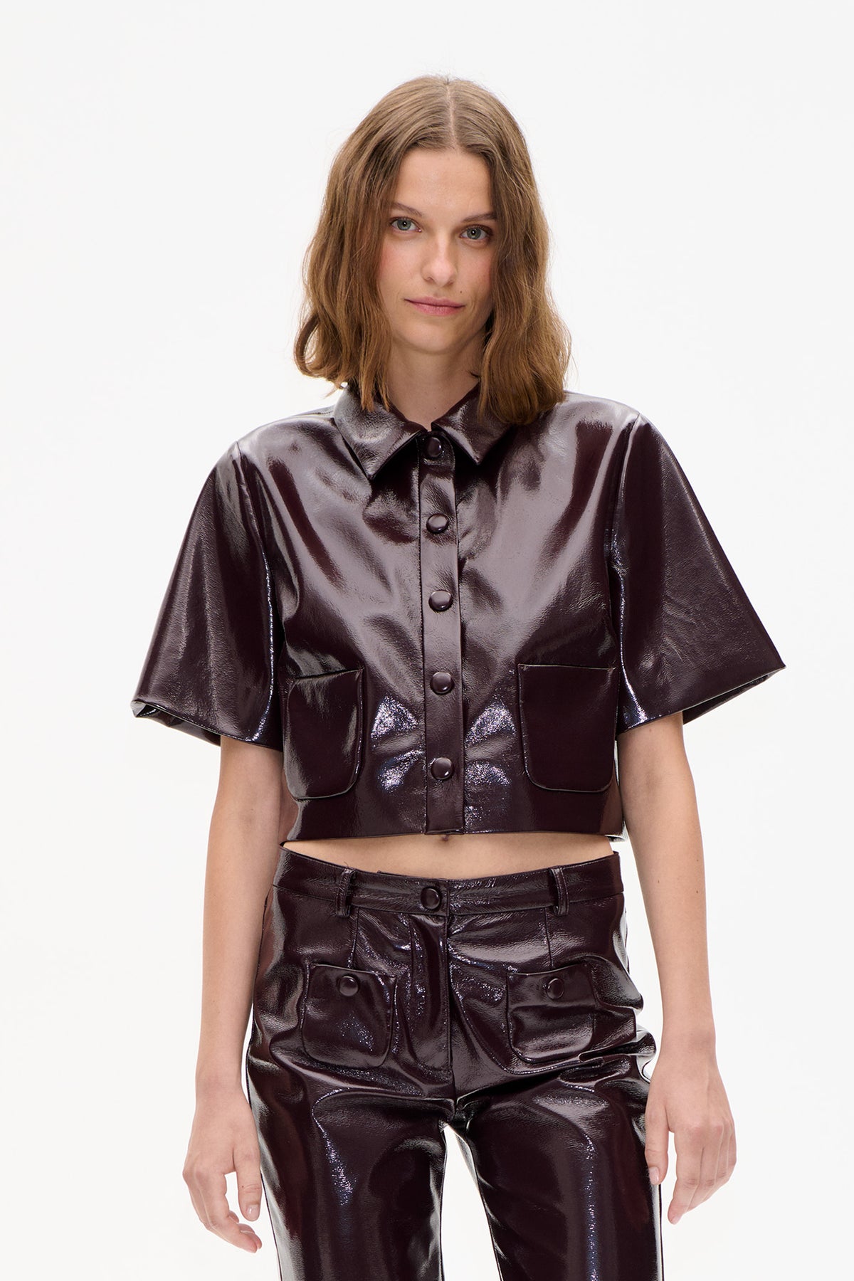 Front view of a model wearing a glossy dark brown short-sleeved button-up shirt with a pointed collar and two flap pockets, paired with matching trousers.