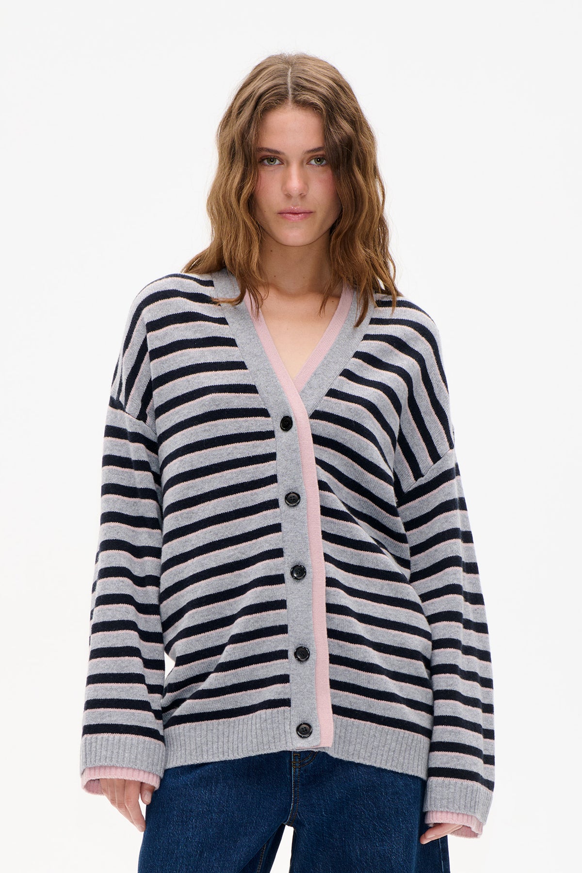 Front view of a model wearing a grey cardigan with navy and pale pink stripes, pink trim and dark buttons.