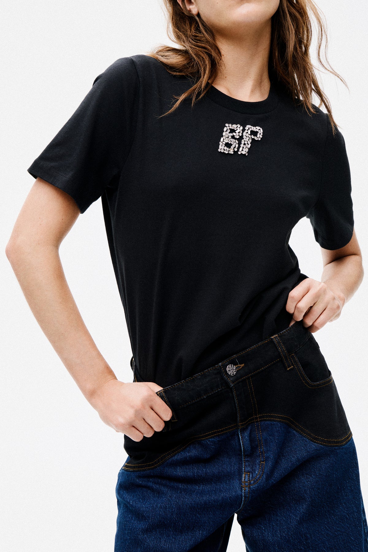 Close campaign view of a model wearing a black short-sleeved crew-neck T-shirt with sparkling crystal lettering and dark blue jeans.