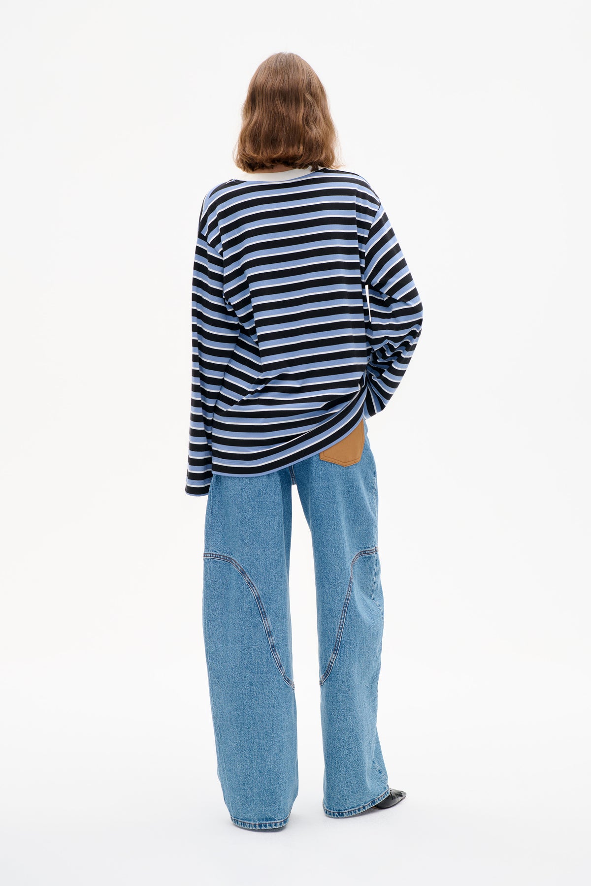 Achteraanzicht van een model met een zwarte, lichtblauwe en witte gestreepte top met lange mouwen en een wijde blauwe jeans.