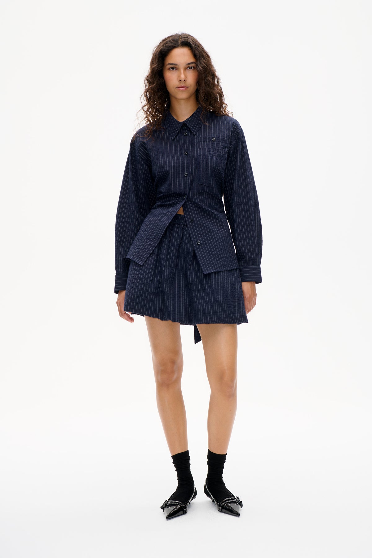 Model wearing a navy pinstriped button-front shirt with chest pockets and matching shorts, shown from the front.