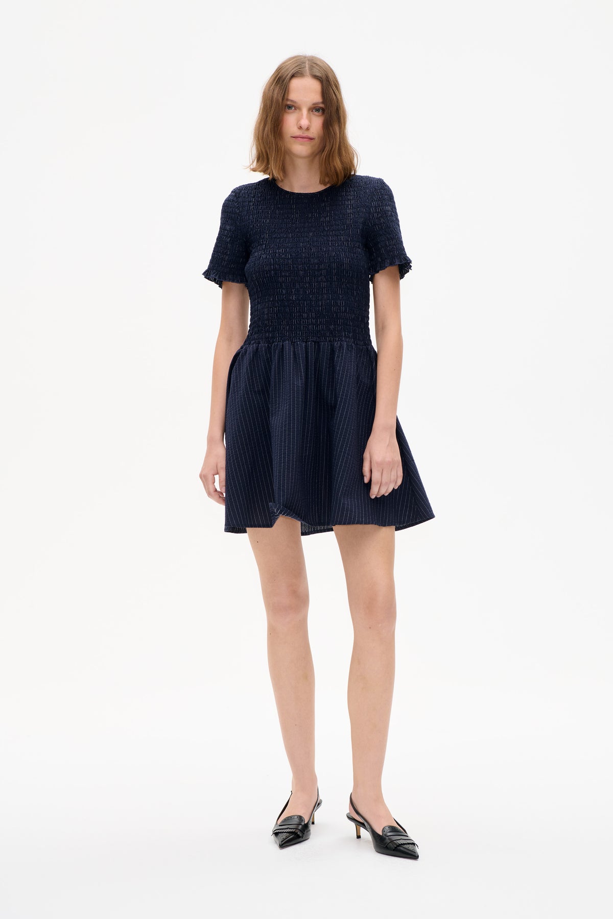 Model wearing a navy dress with a textured bodice, ruffled short sleeves and a fine pinstriped skirt, front view.