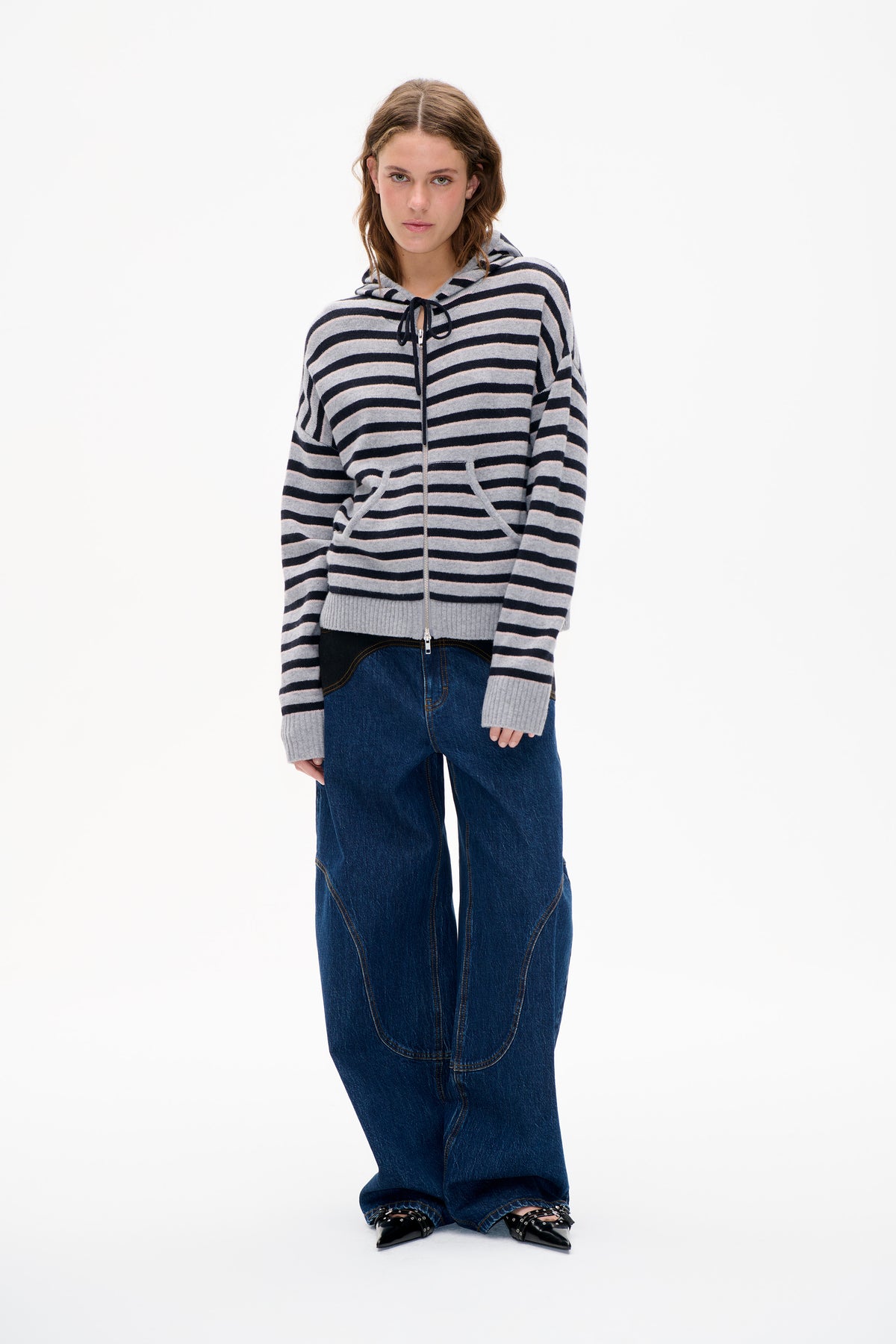 Front view of a model wearing a grey hooded zip-up sweater with navy and pale pink horizontal stripes and ribbed cuffs.