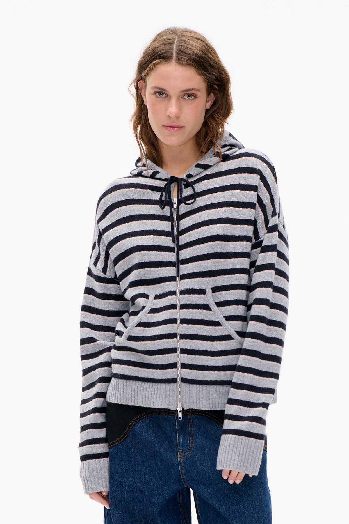 Front view of a model wearing a grey and black striped hooded knit jacket with a front zip and drawstrings.