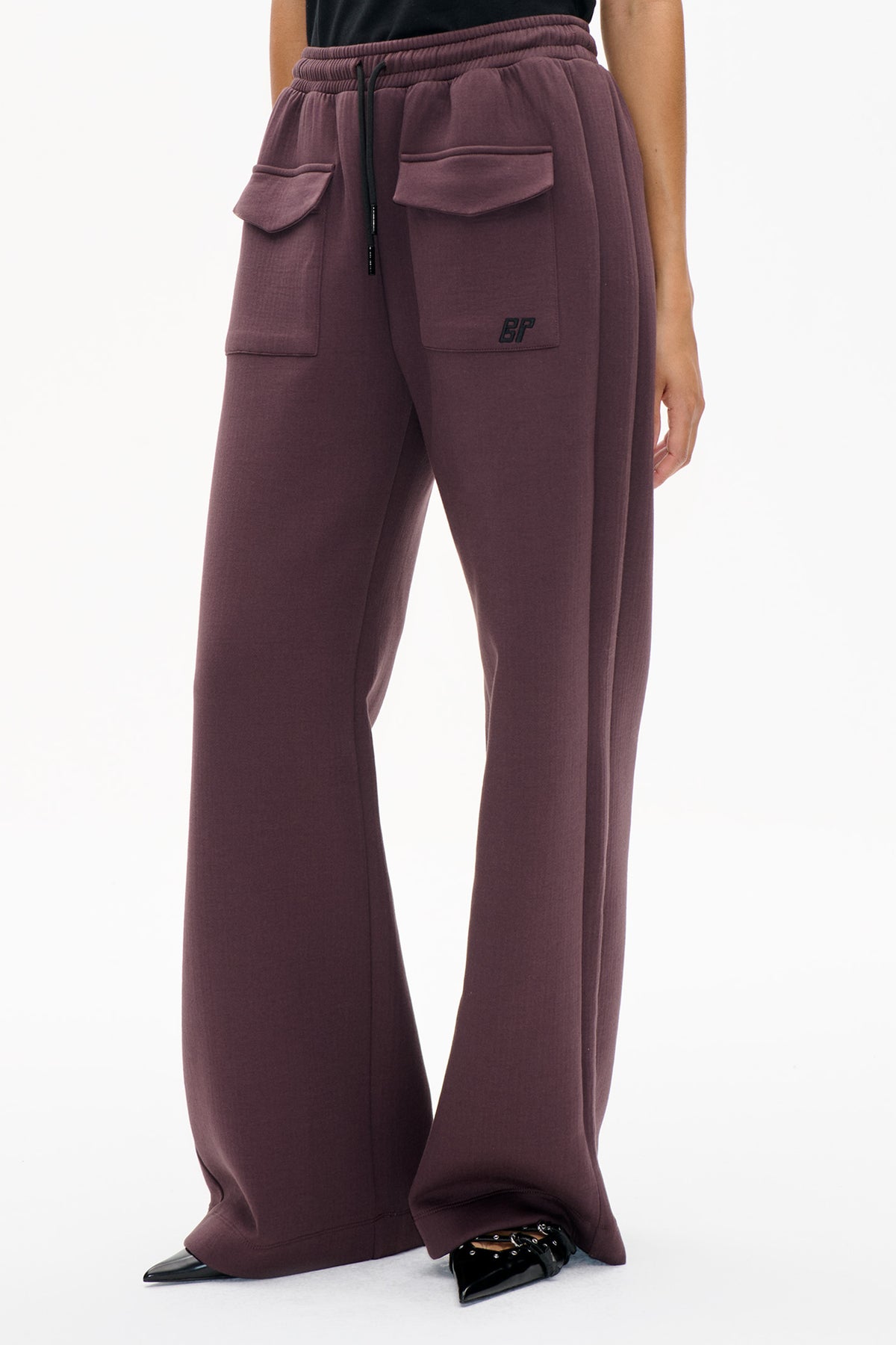 Front detail of plum wide-leg sweatpants with a ribbed drawstring waistband, large flap pockets and a small embroidered BP logo.