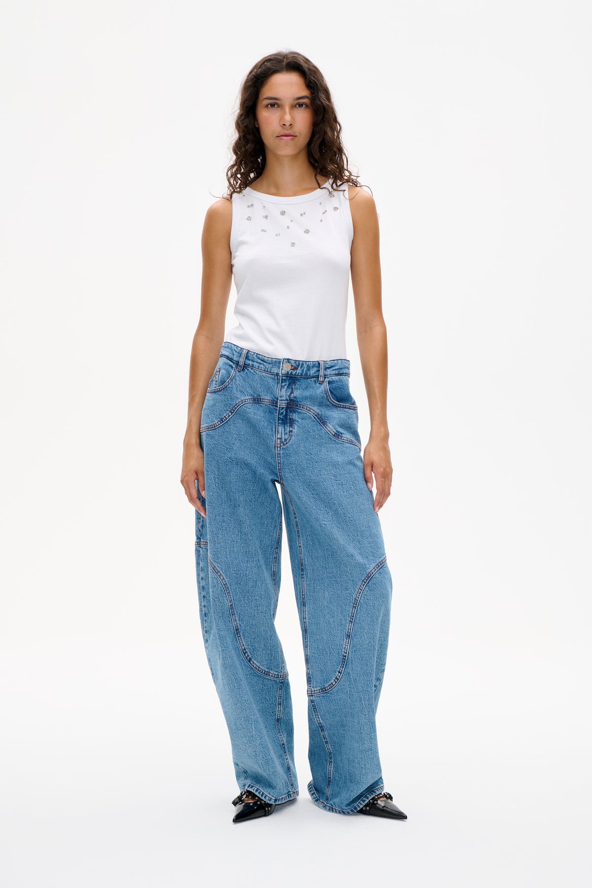 Front view of a white sleeveless top with scattered sparkling embellishments, styled with light blue wide-leg jeans.