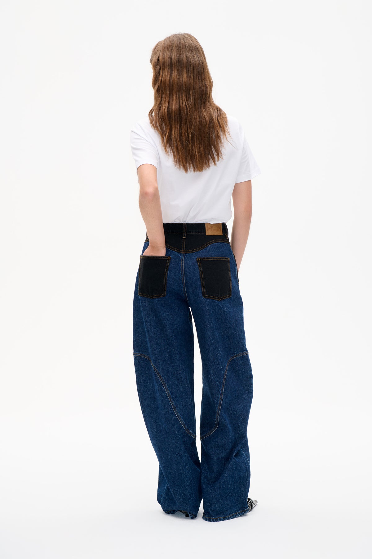 Back view of a model wearing a white short-sleeved T-shirt and wide-leg blue jeans with black contrast panels and patch pockets.