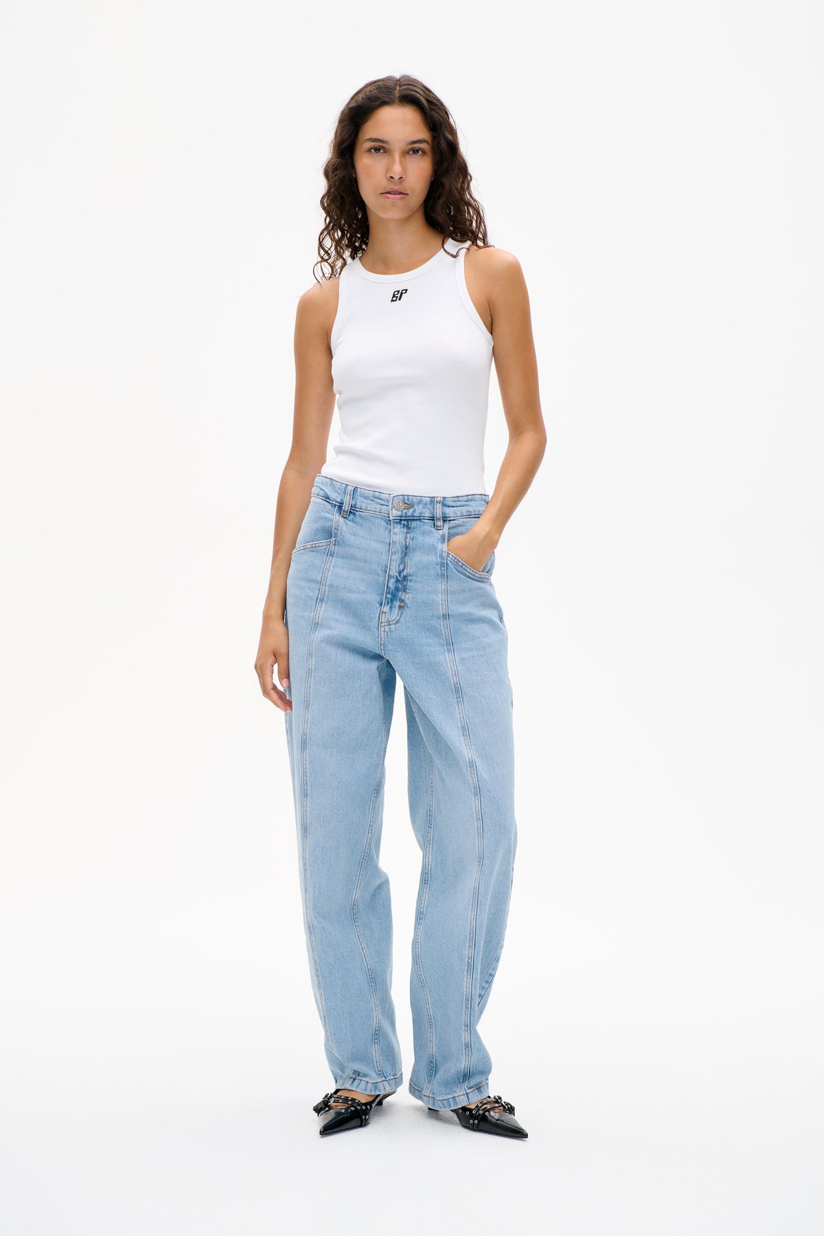 Model wearing a white ribbed sleeveless top with a small chest logo and light-wash wide-leg jeans, shown from the front.