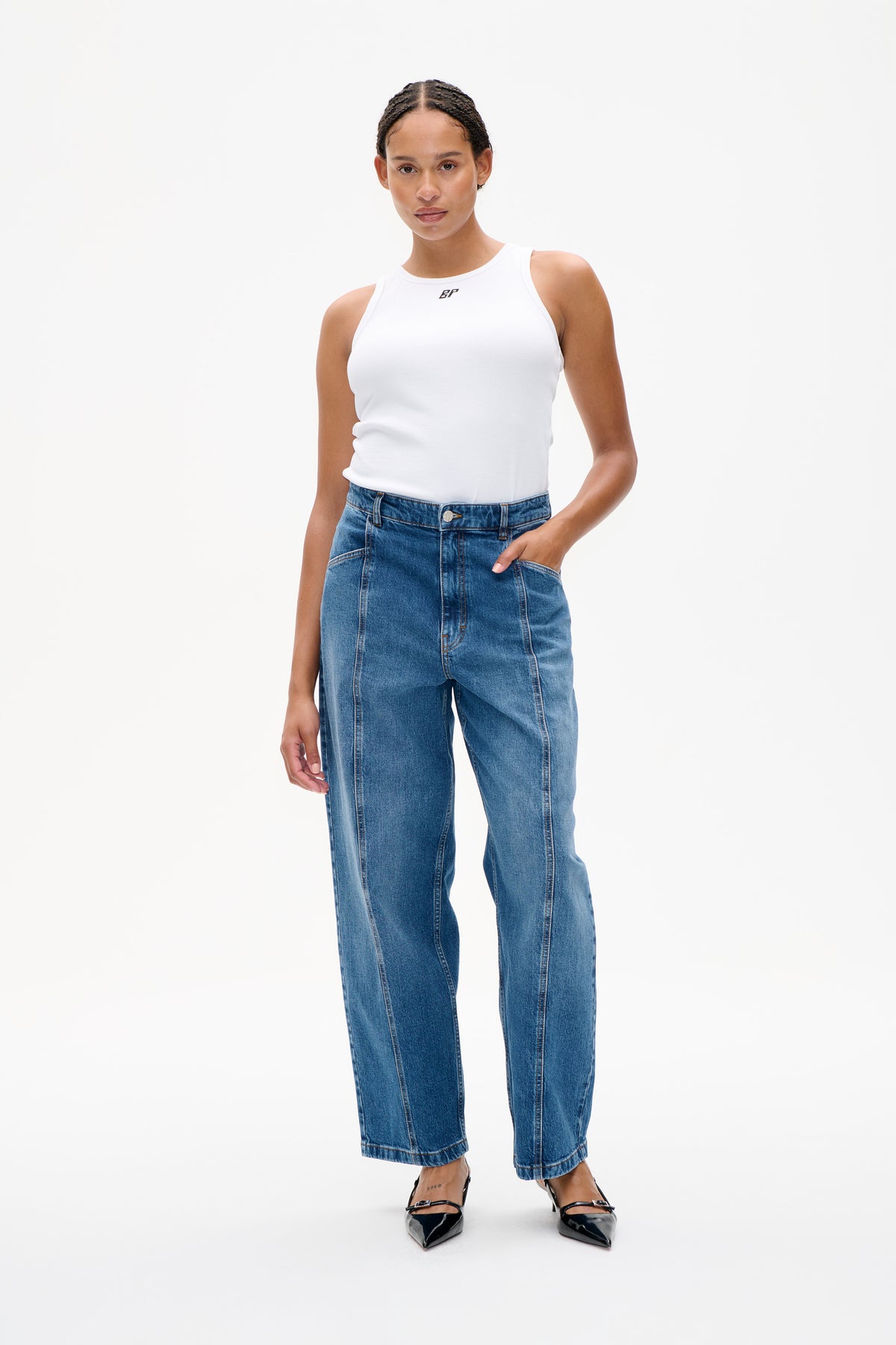 Model draagt een witte, mouwloze ribgebreide top met een klein logo op de borst en blauwe jeans met wijde pijpen, gezien van voren.