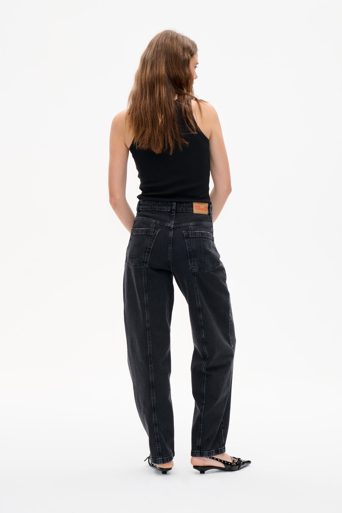 Achteraanzicht van een model met een zwarte mouwloze top en een donker antraciet gewassen jeans met achterzakken en wijde pijpen.