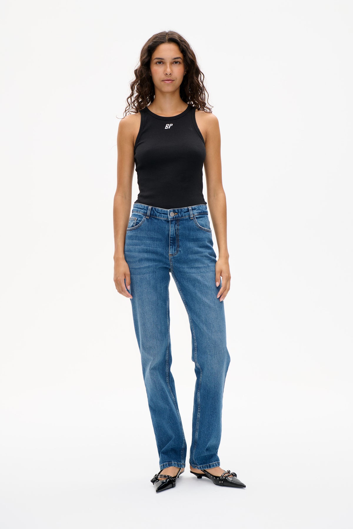 Front view of a black sleeveless ribbed top with a small white chest logo, styled with blue jeans.