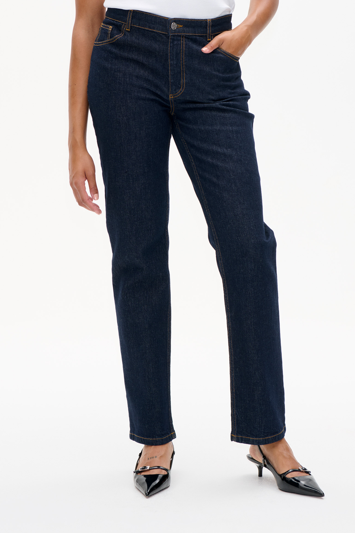 Front view of dark indigo straight-leg jeans with contrast stitching, worn with a white top and black pointed heels.
