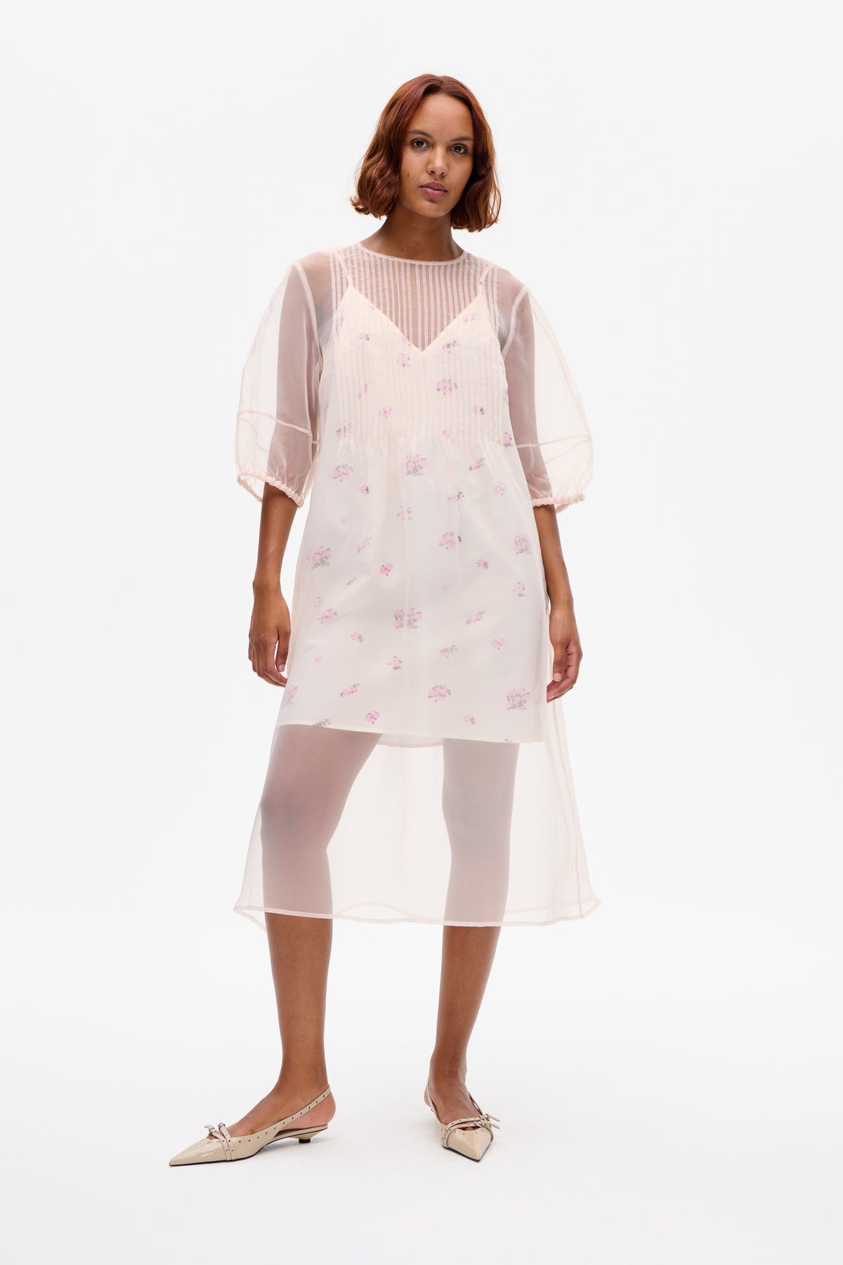 Front view of a sheer ivory knee-length dress with vertical stripes, scattered pink floral print, and voluminous three-quarter sleeves.