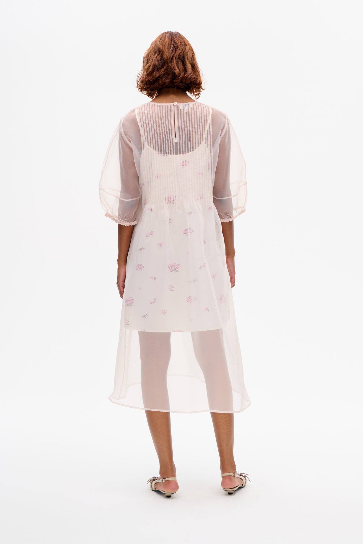 Back view of a sheer pale pink floral-print dress with a striped yoke, puff sleeves and a long translucent hem.