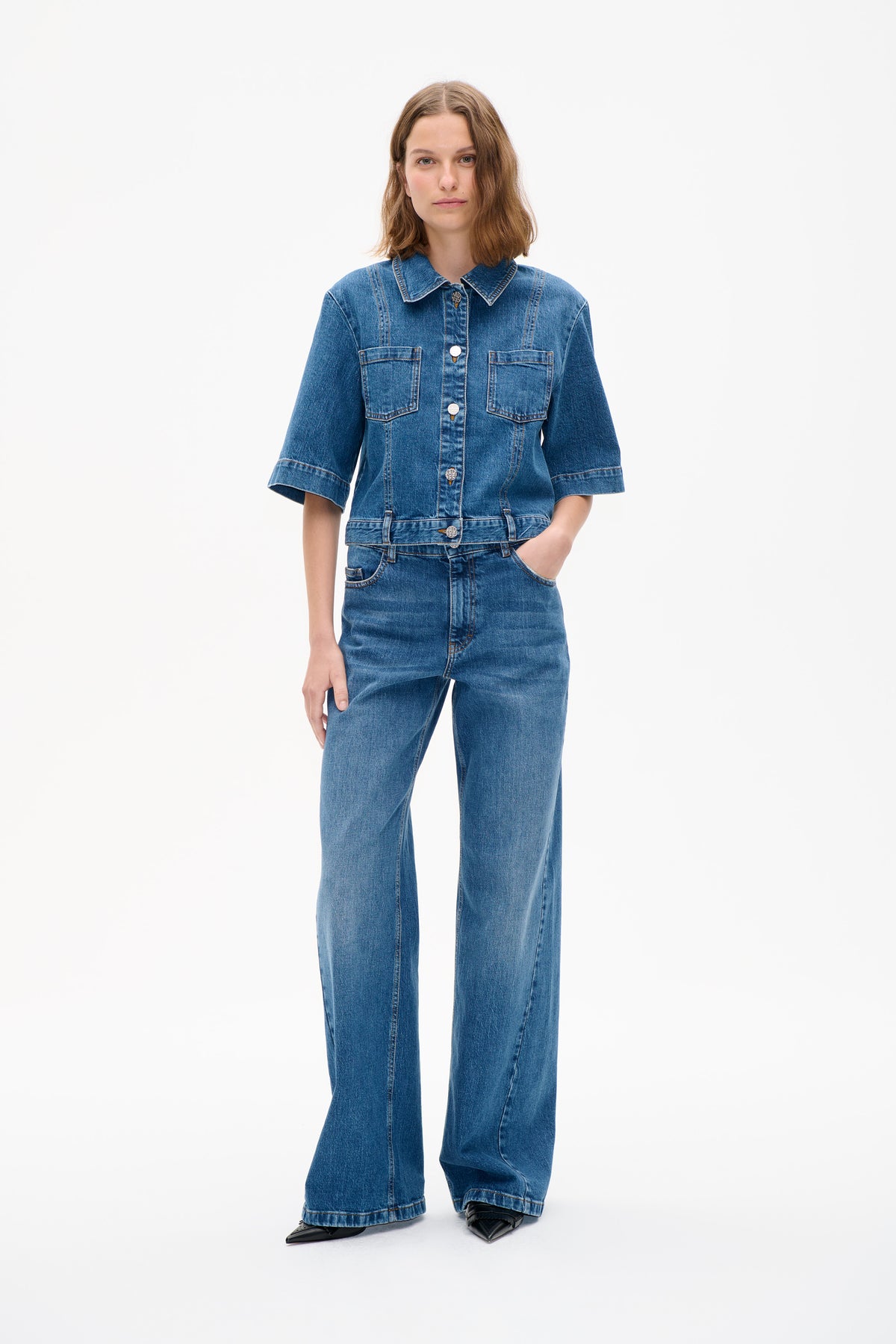 Front view of a model wearing a blue denim jacket with short sleeves and chest pockets, paired with matching wide-leg jeans.
