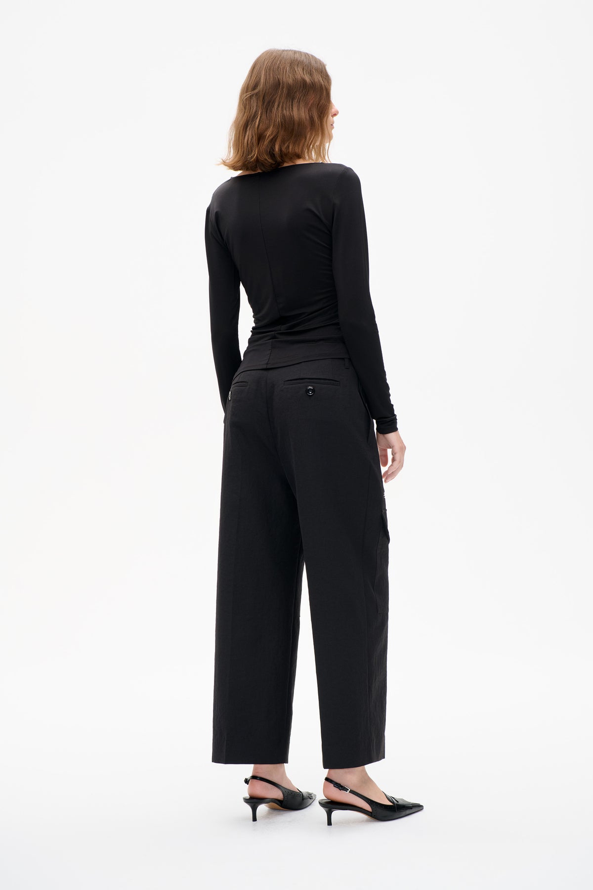 Rear view of a model wearing a fitted black long-sleeve top and cropped wide-leg trousers with buttoned welt back pockets.