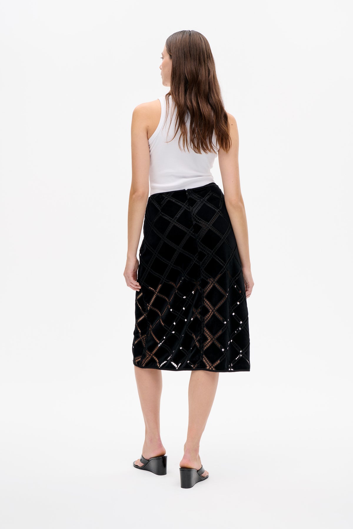 Rear view of a model wearing a white ribbed sleeveless top and black knee-length skirt with a geometric openwork lattice pattern.