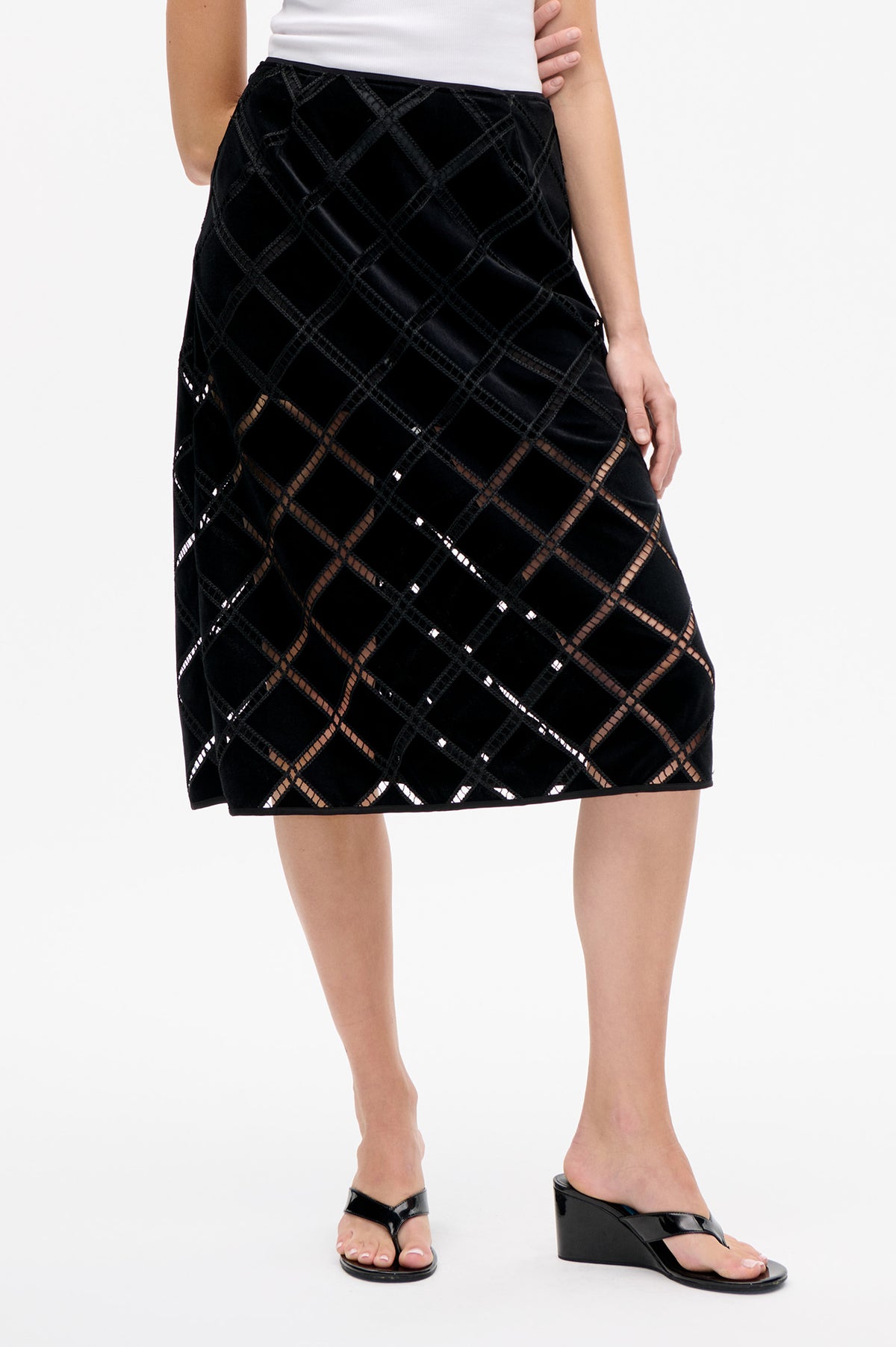 Close-up front view of a black knee-length skirt with a geometric diamond pattern, glossy panels and sheer openwork lines.