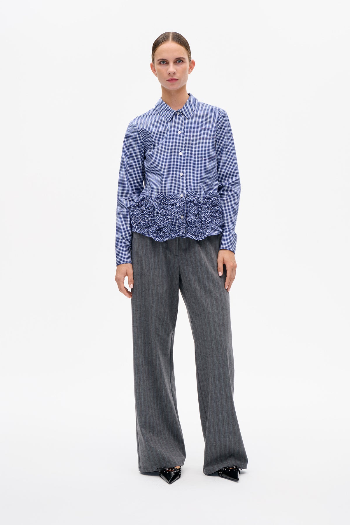 Front view of a blue-and-white gingham button-up shirt with a ruffled hem, paired with gray wide-leg trousers.