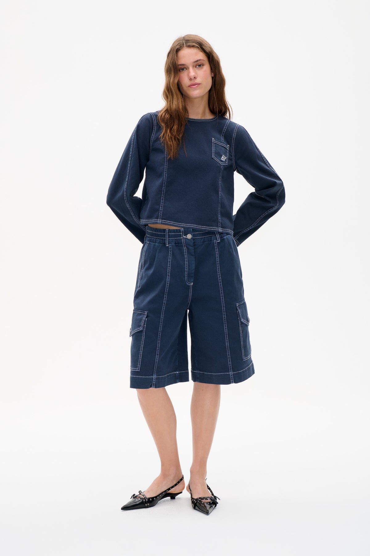 Front view of a model wearing a navy long-sleeved top with a chest pocket and matching cargo shorts, both with white contrast stitching.