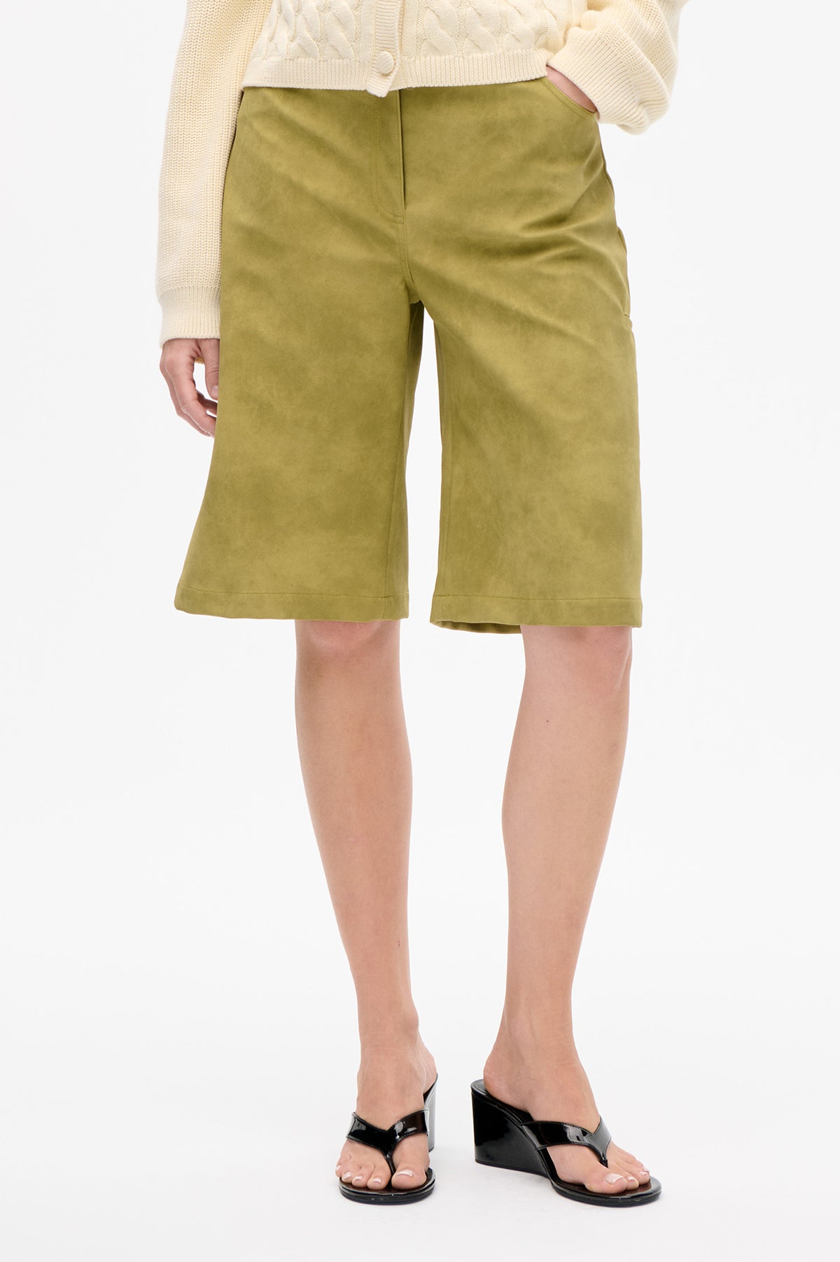 Front detail of olive-green knee-length wide-leg shorts with slanted pockets, styled with a cream cable-knit cardigan.