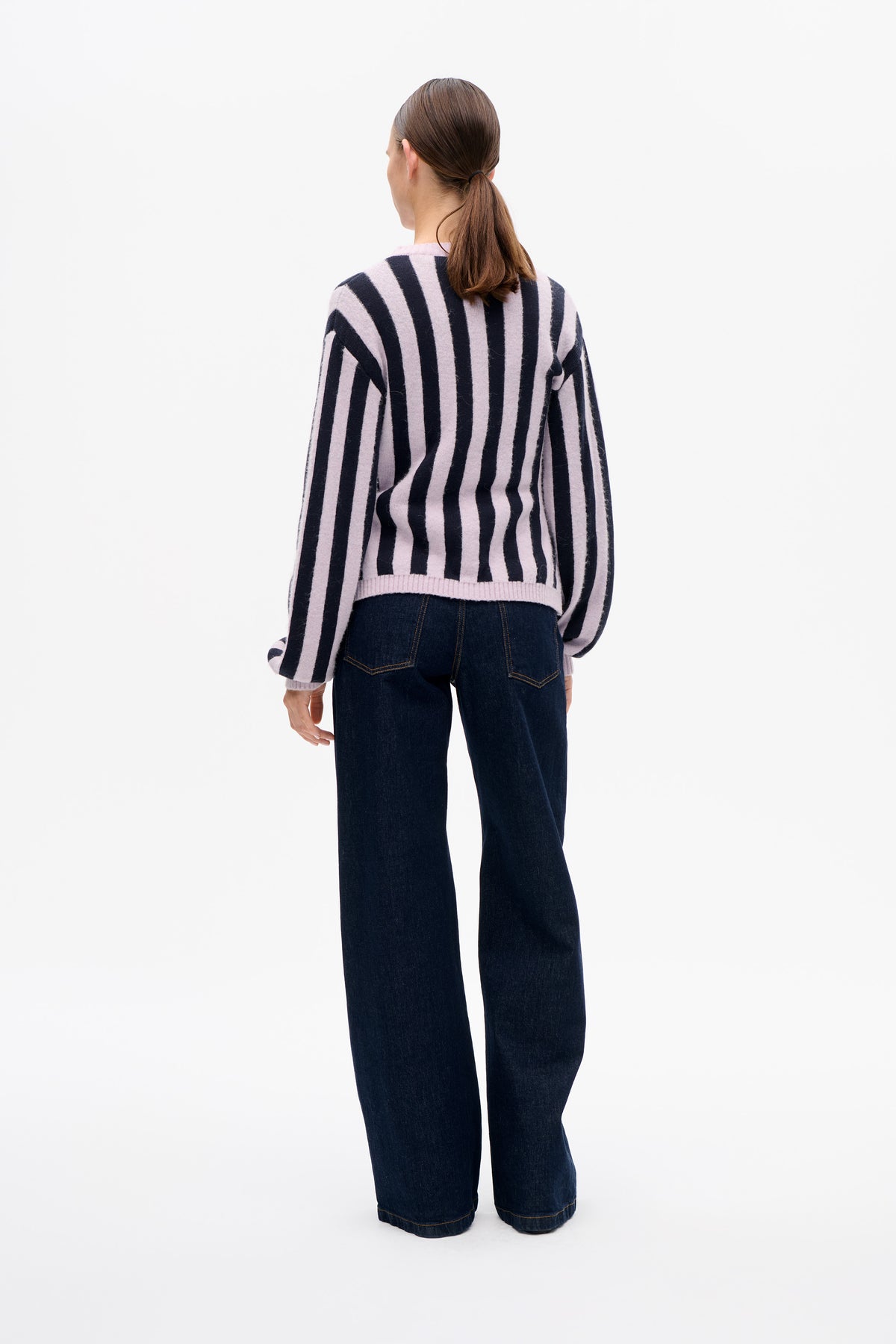 Back view of a model wearing a lilac and dark navy striped sweater with dark wide-leg jeans.