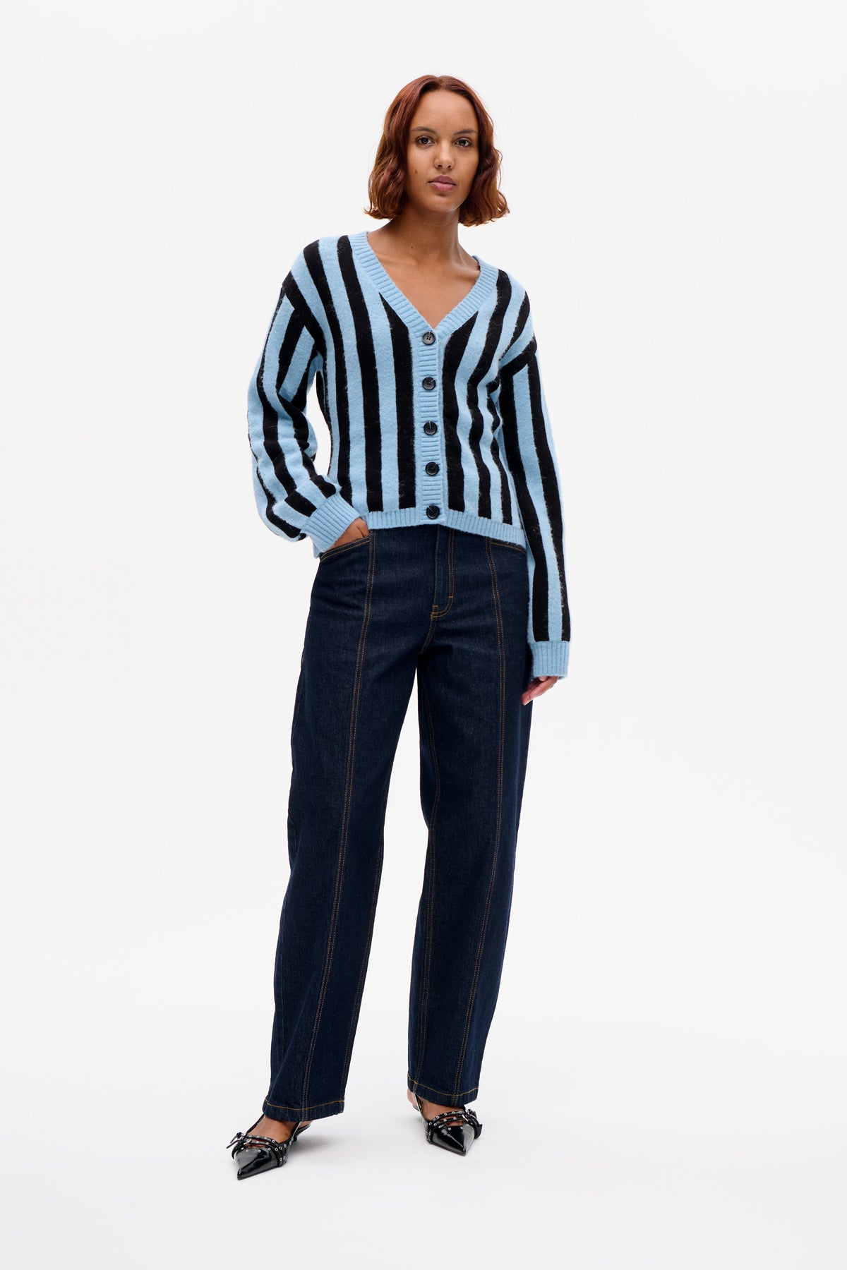 Front view of a model wearing a light blue and black striped V-neck cardigan with dark buttons and dark jeans.