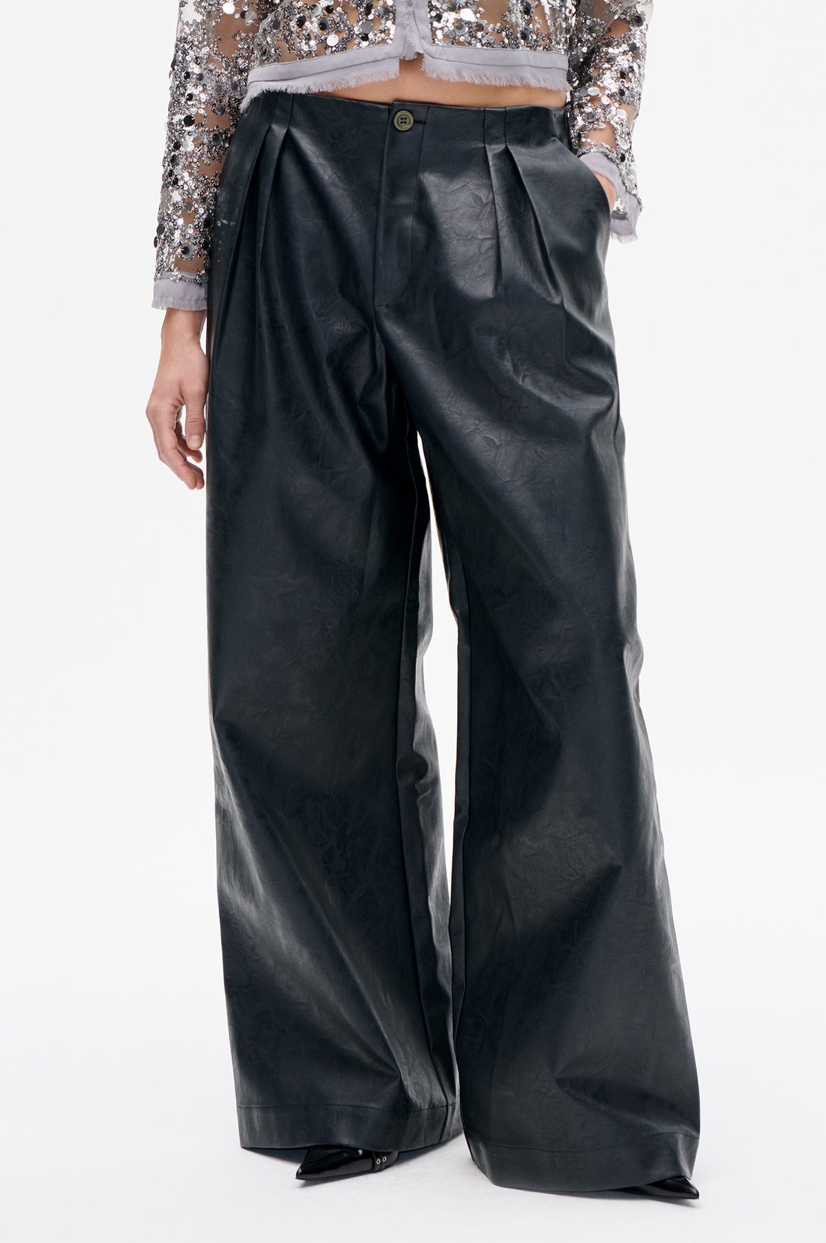 Close-up front view of black wide-leg trousers with a buttoned waist and pleats, worn with a silver sequin top.