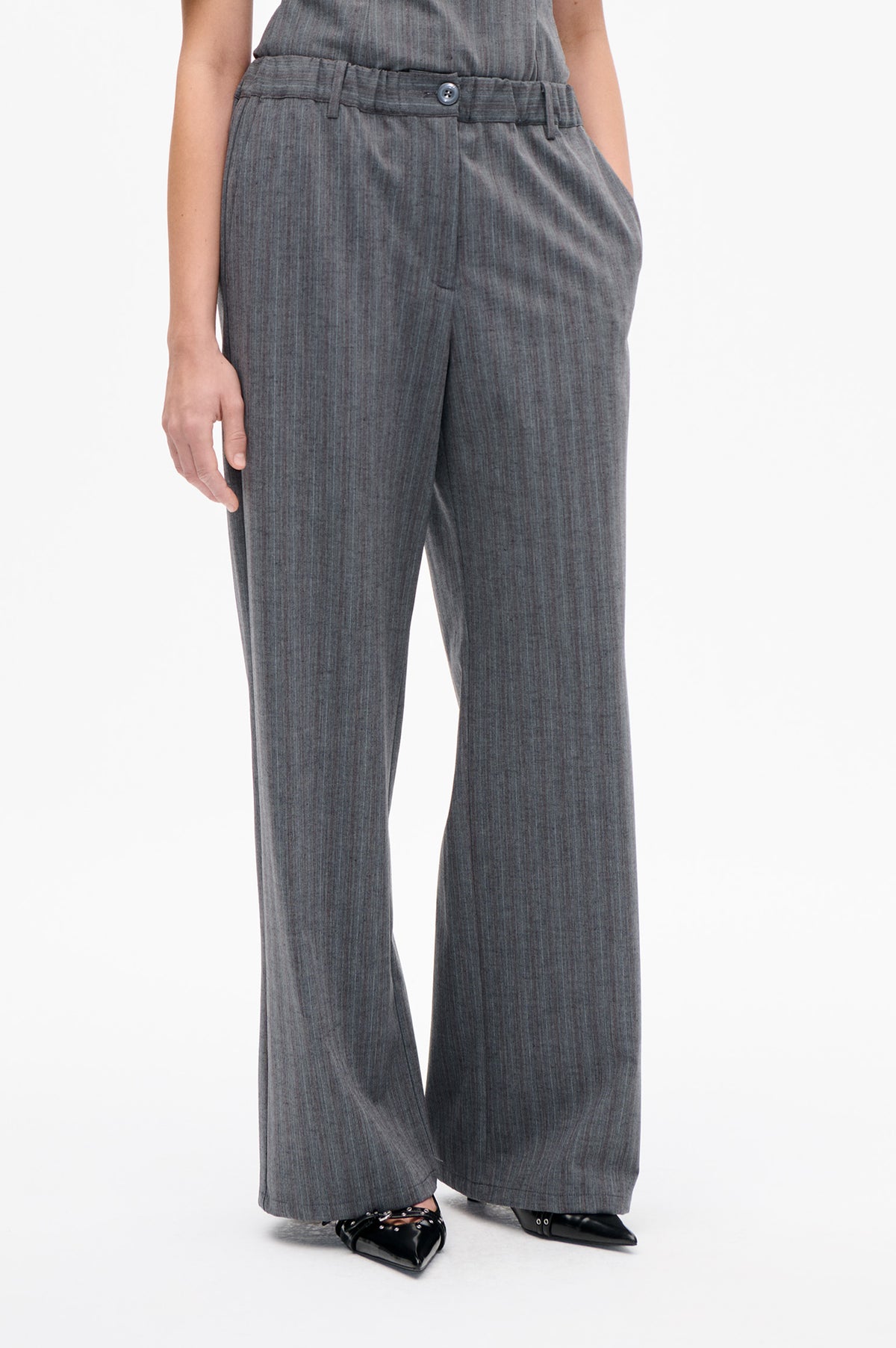 Front detail of charcoal grey wide-leg trousers with fine vertical stripes, belt loops and a buttoned waistband.