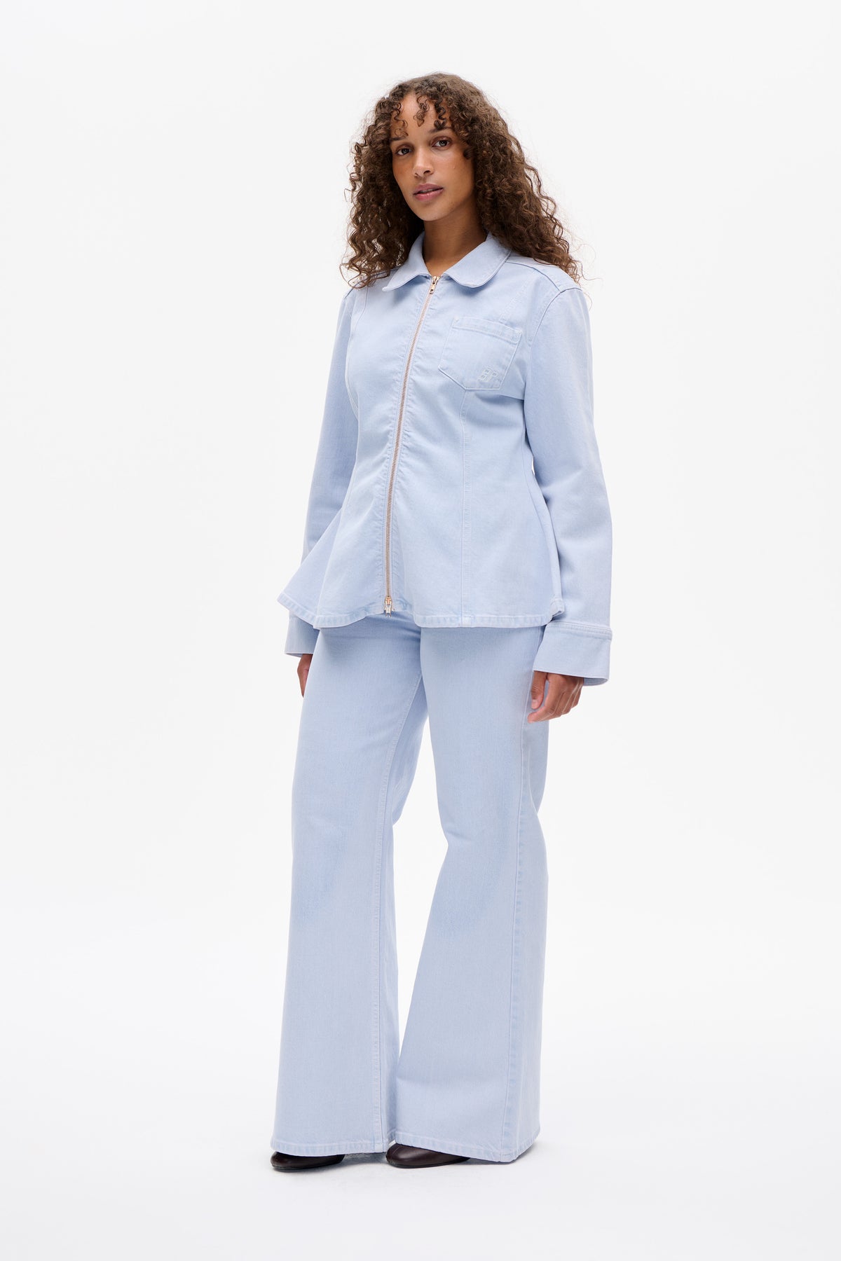 Model wearing a pale blue zip-front jacket with a rounded collar and chest pocket, paired with matching wide-leg trousers.