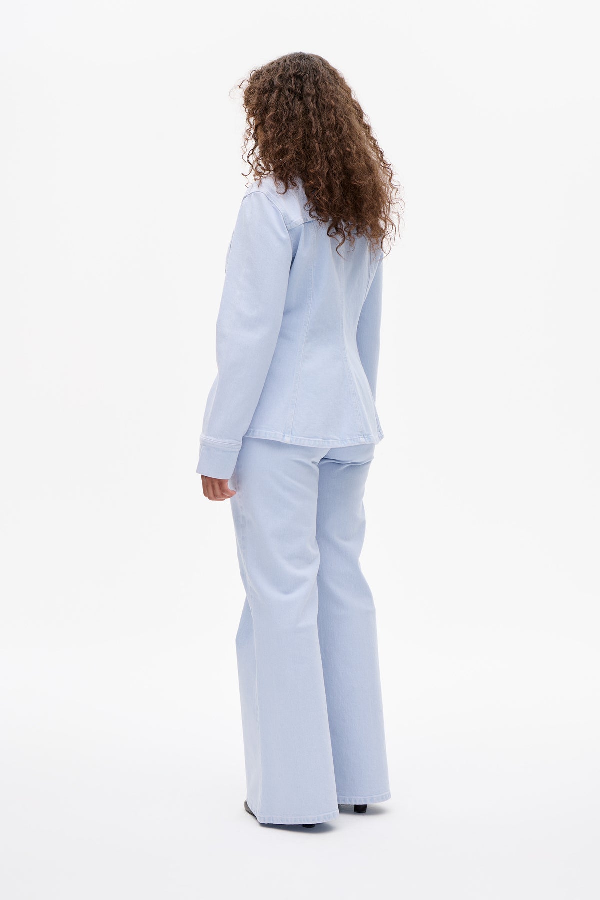 Rear view of a model wearing a pale blue denim jacket and matching wide-leg jeans against a white background.
