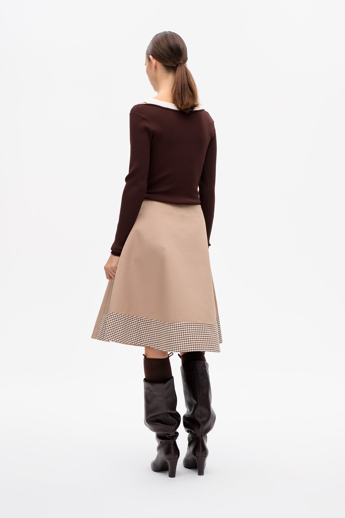 Back view of a model wearing a dark brown ribbed long-sleeve top and beige skirt with a brown-and-cream checked hem