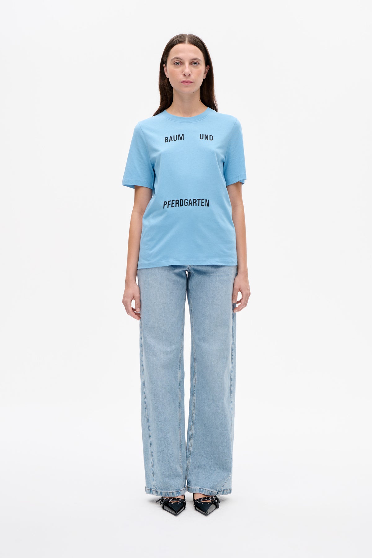 Model wearing a light blue short-sleeved T-shirt with black Baum und Pferdgarten lettering, paired with light-wash wide-leg jeans.