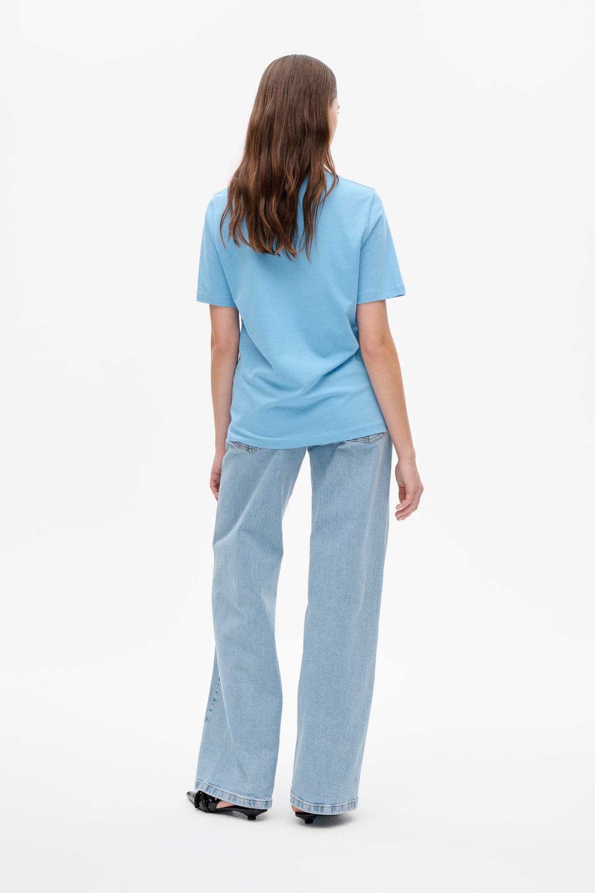 Back view of a model wearing a plain light blue short-sleeved T-shirt with light-wash wide-leg jeans.