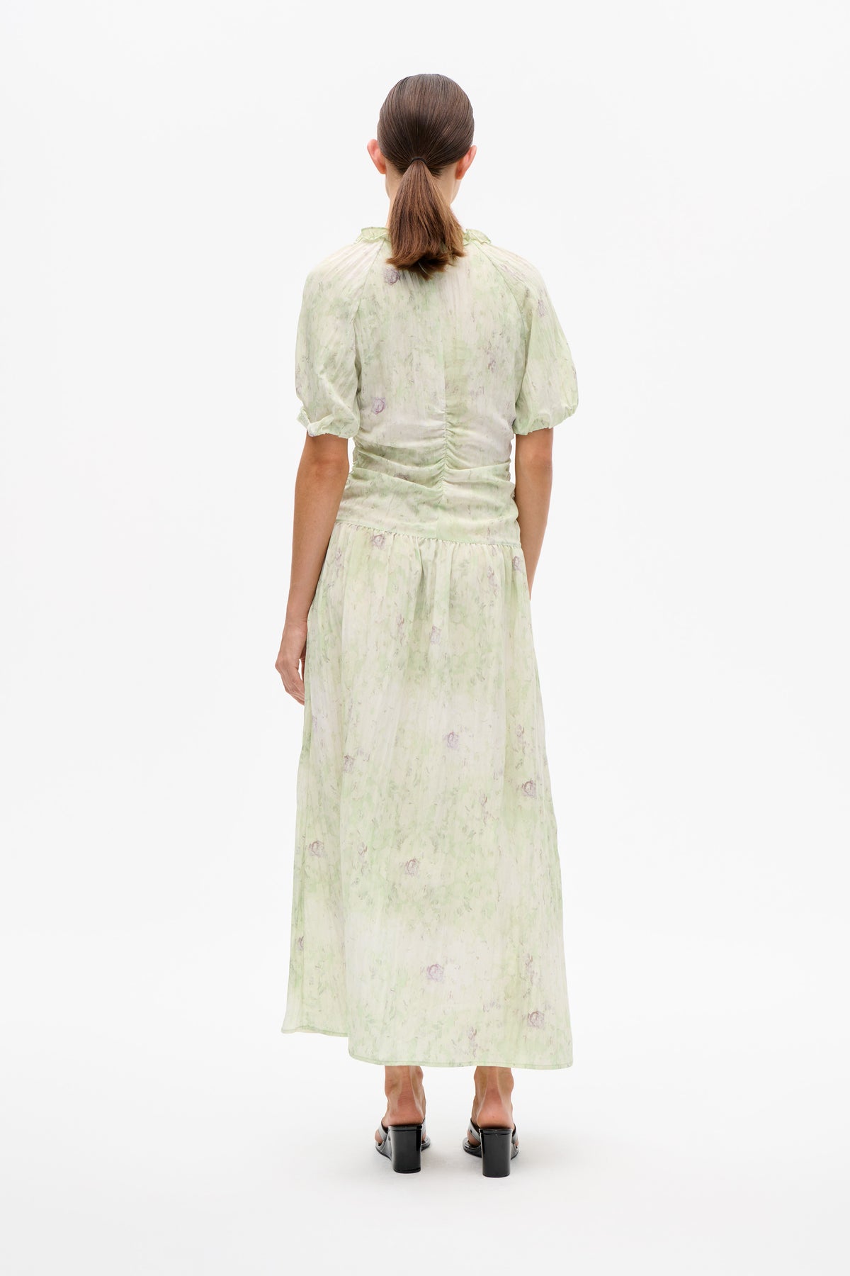 Back view of a pale green and cream floral midi dress with short puff sleeves, a ruffled neckline and gathered waist.