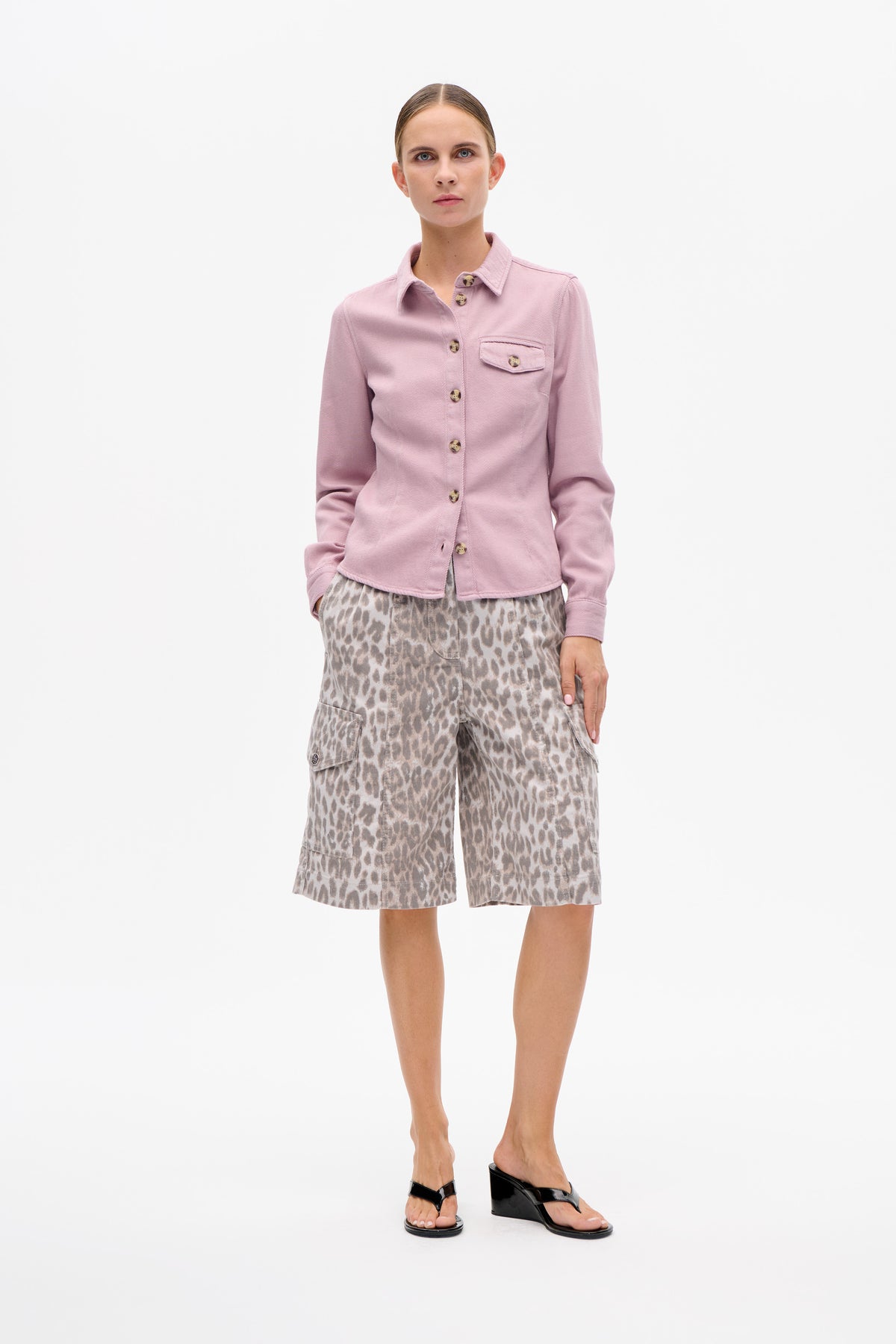 Model wearing a dusty pink button-front shirt with a chest pocket and beige leopard-print knee-length shorts, shown from the front against a white background.