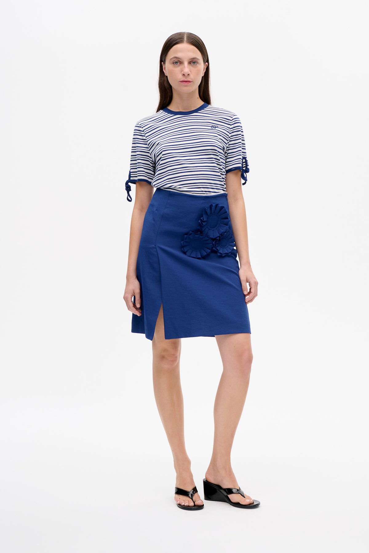 Model wearing a white and navy striped T-shirt with tie-detail sleeves and a cobalt blue skirt with floral appliqués and a front slit.