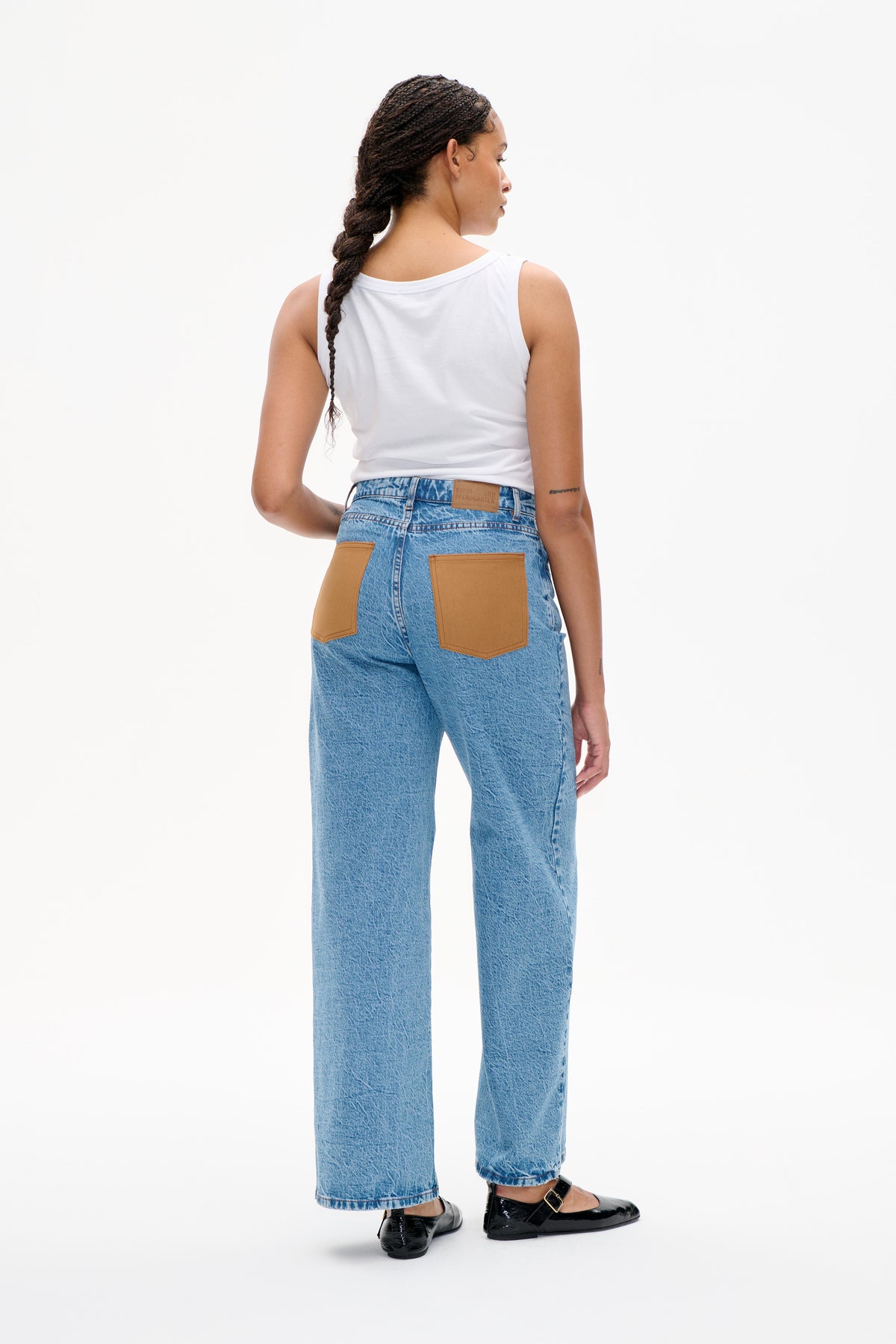 Back view of light blue jeans with oversized tan patch pockets, styled with a white sleeveless top and black flats.