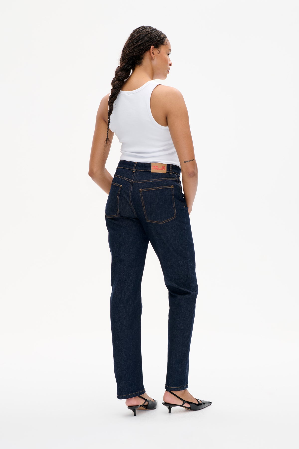 Model viewed from behind wearing a white sleeveless top and dark indigo straight-leg jeans with contrast stitching and back pockets.