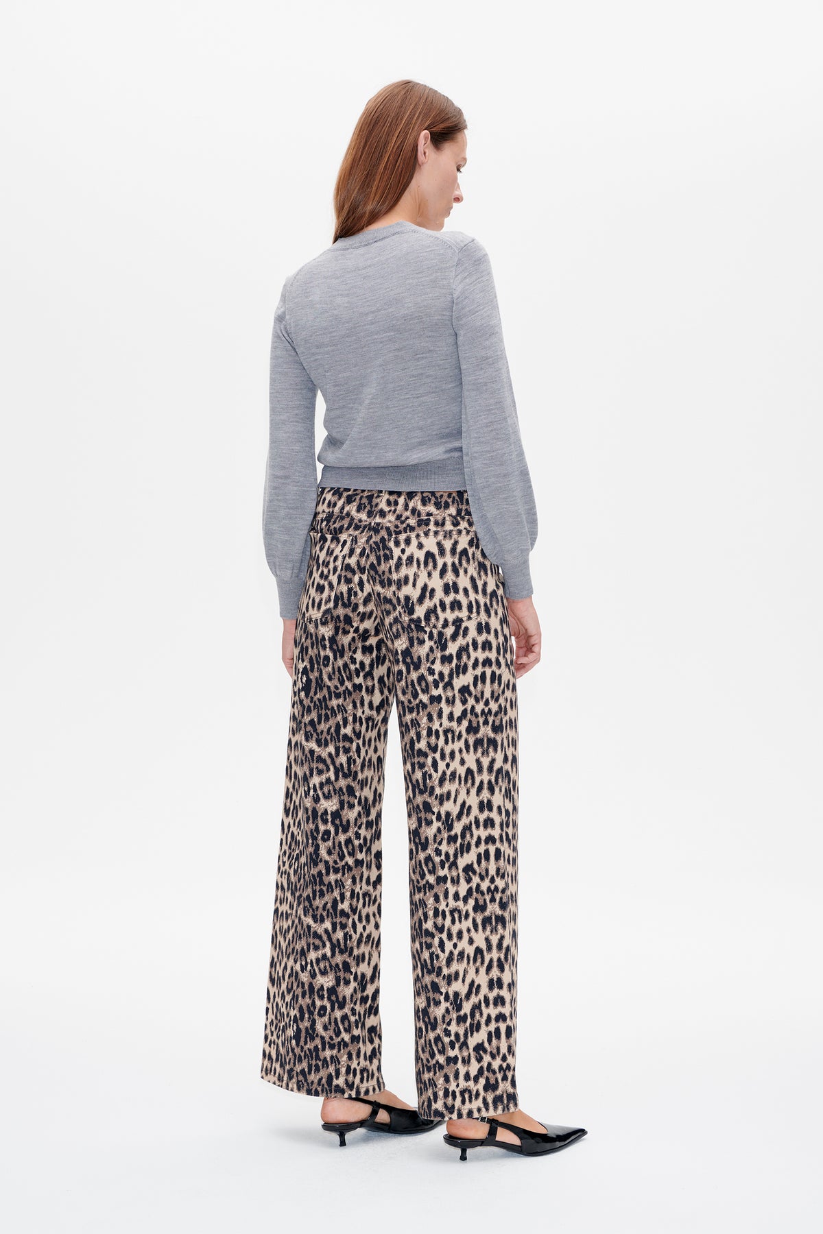Back view of a model wearing a light grey long-sleeved sweater with ribbed cuffs and hem, paired with beige and black leopard-print trousers.