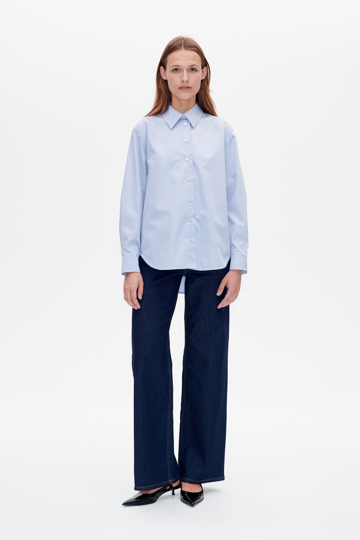 Front view of a model wearing a light blue button-front shirt with a pointed collar, dark wide-leg jeans and black heels.