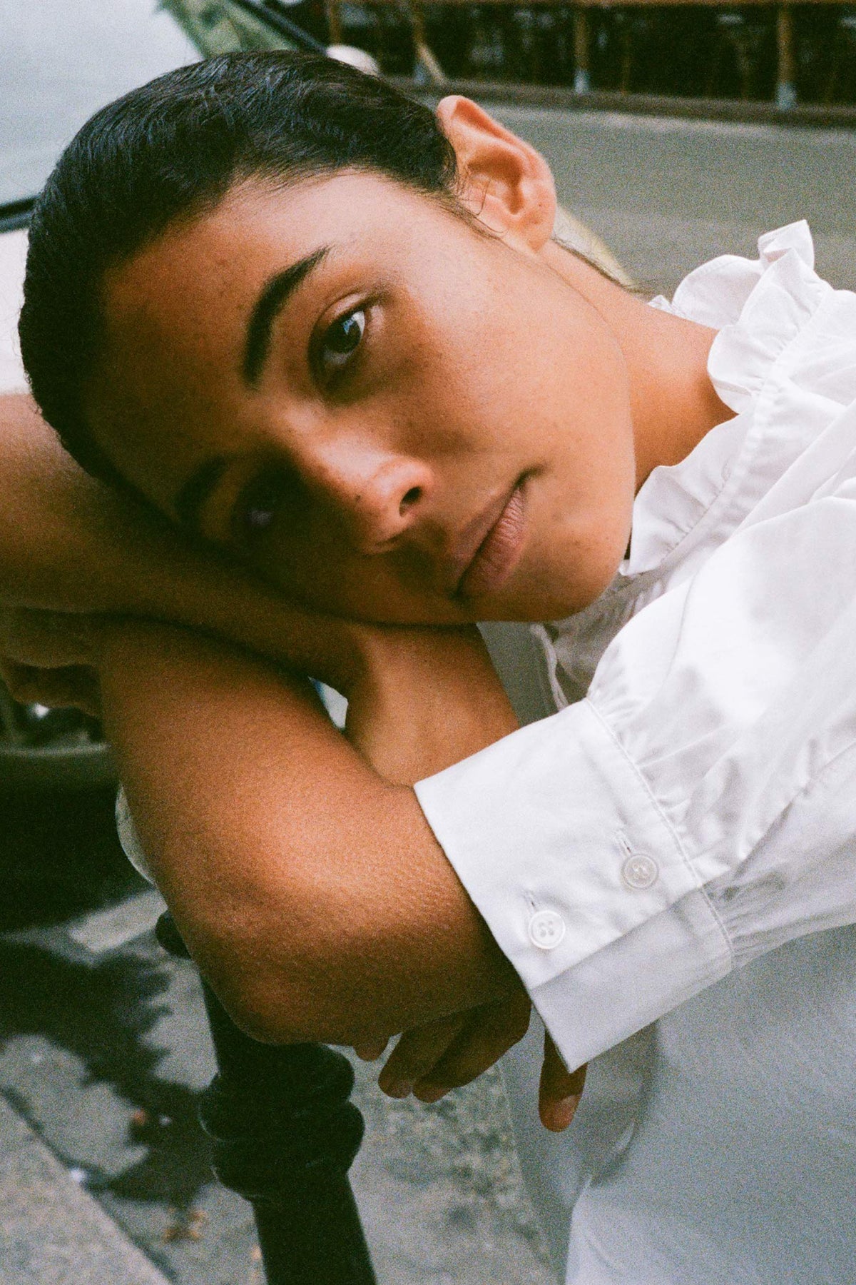 Close-up campaign portrait of a reclining model wearing a white button-front blouse with ruffled sleeves