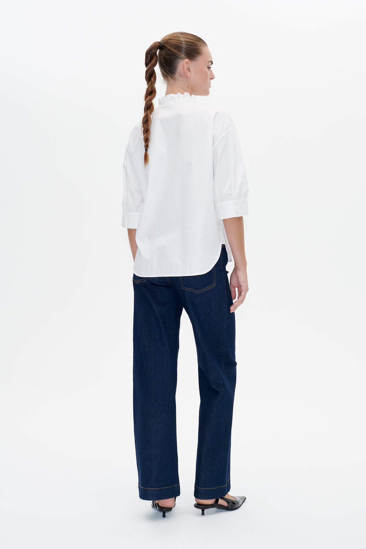 Back view of a white blouse with a ruffled collar and elbow-length sleeves, paired with dark indigo wide-leg jeans.