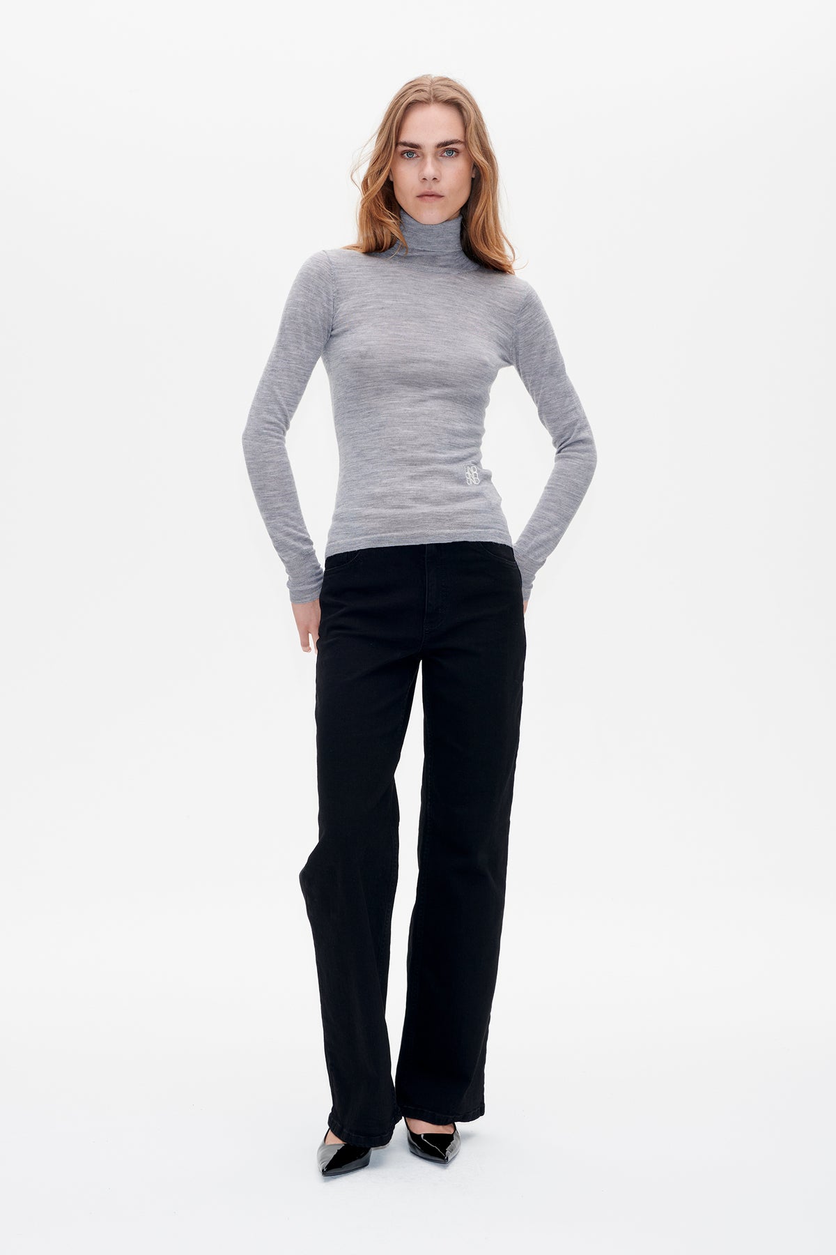 Front view of a model wearing a heather gray fitted long-sleeve turtleneck with a small white waist emblem and black wide-leg trousers.